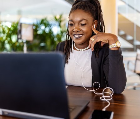 Woman working on computer and listening to headphones connected to phone